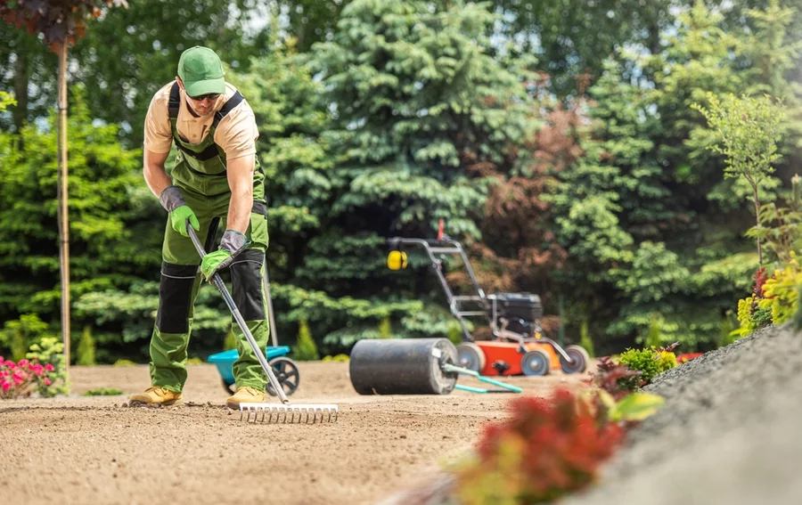 A professional landscaper rakes a garden bed.
